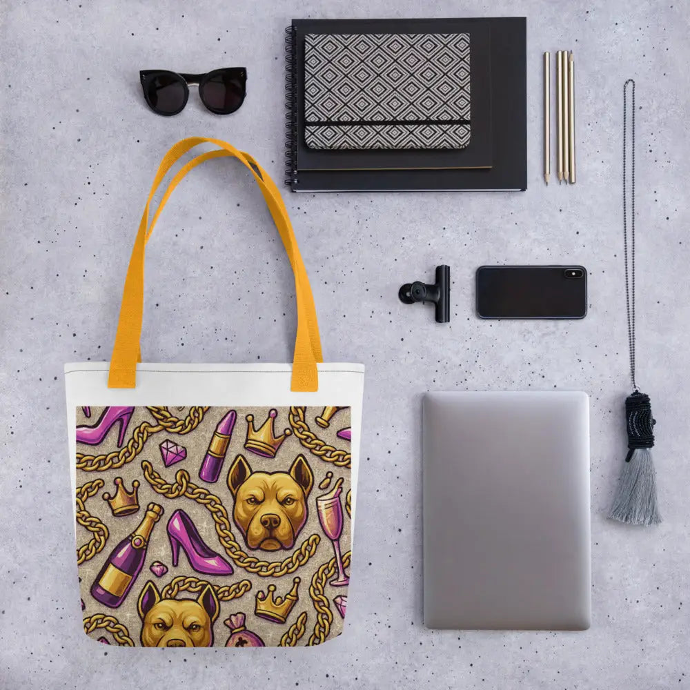 Glamour Pitbull Tote Bag with gold chains, crowns, champagne glasses, high heels print and yellow-orange straps next to sunglasses, notebook, phone, and laptop.